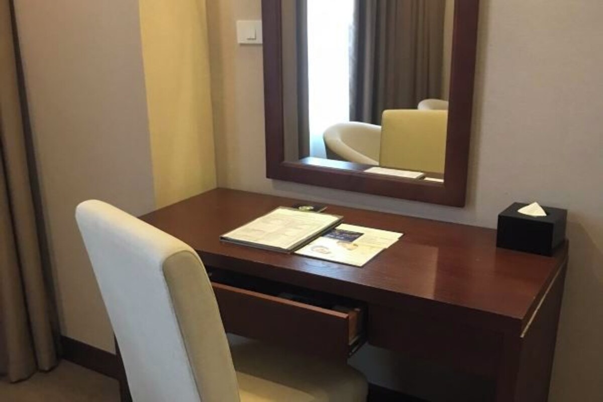 A hotel room with a wooden desk, a chair, a mirror, and a window with curtains.