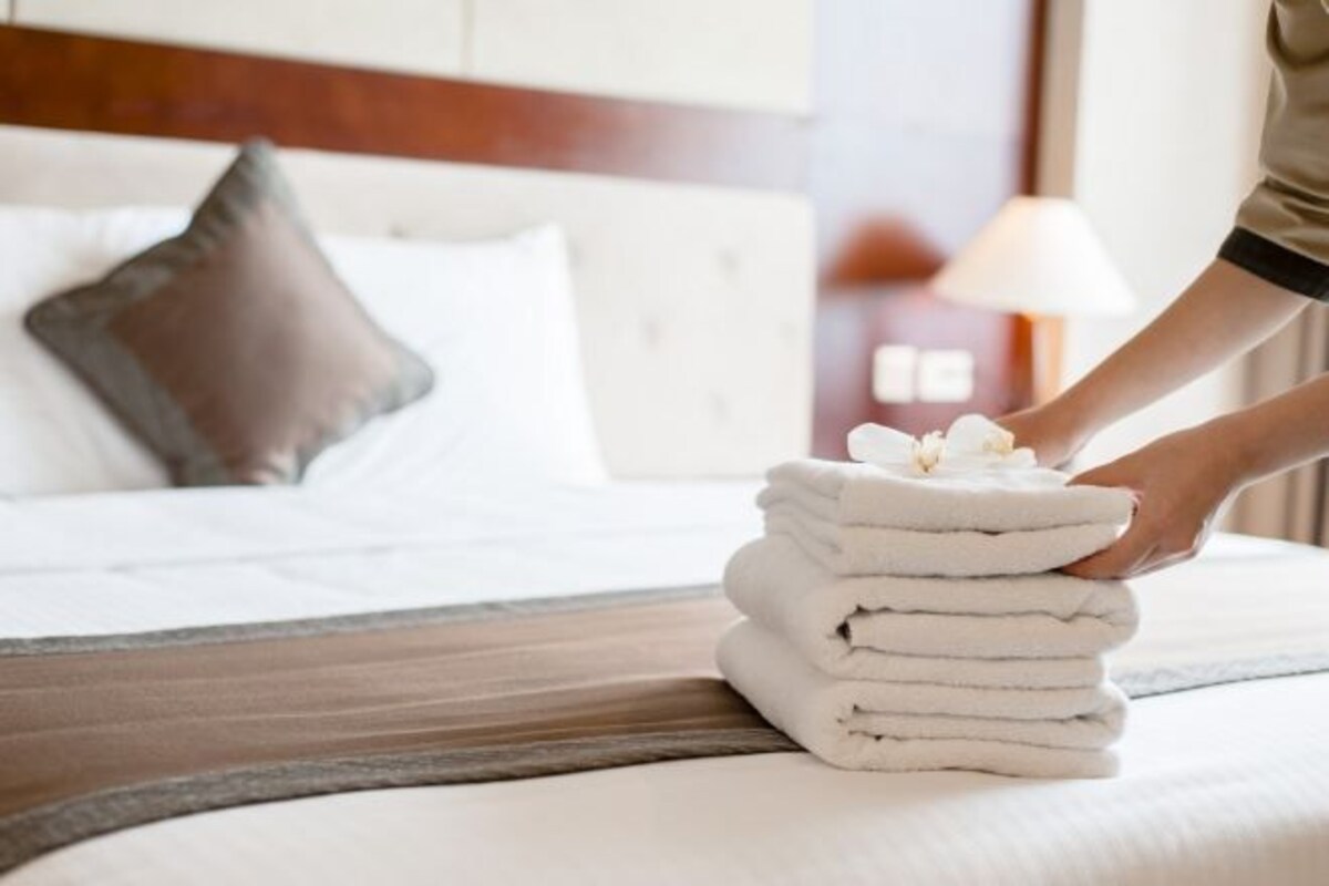 A neatly made bed with a stack of folded towels and a single flower on top.