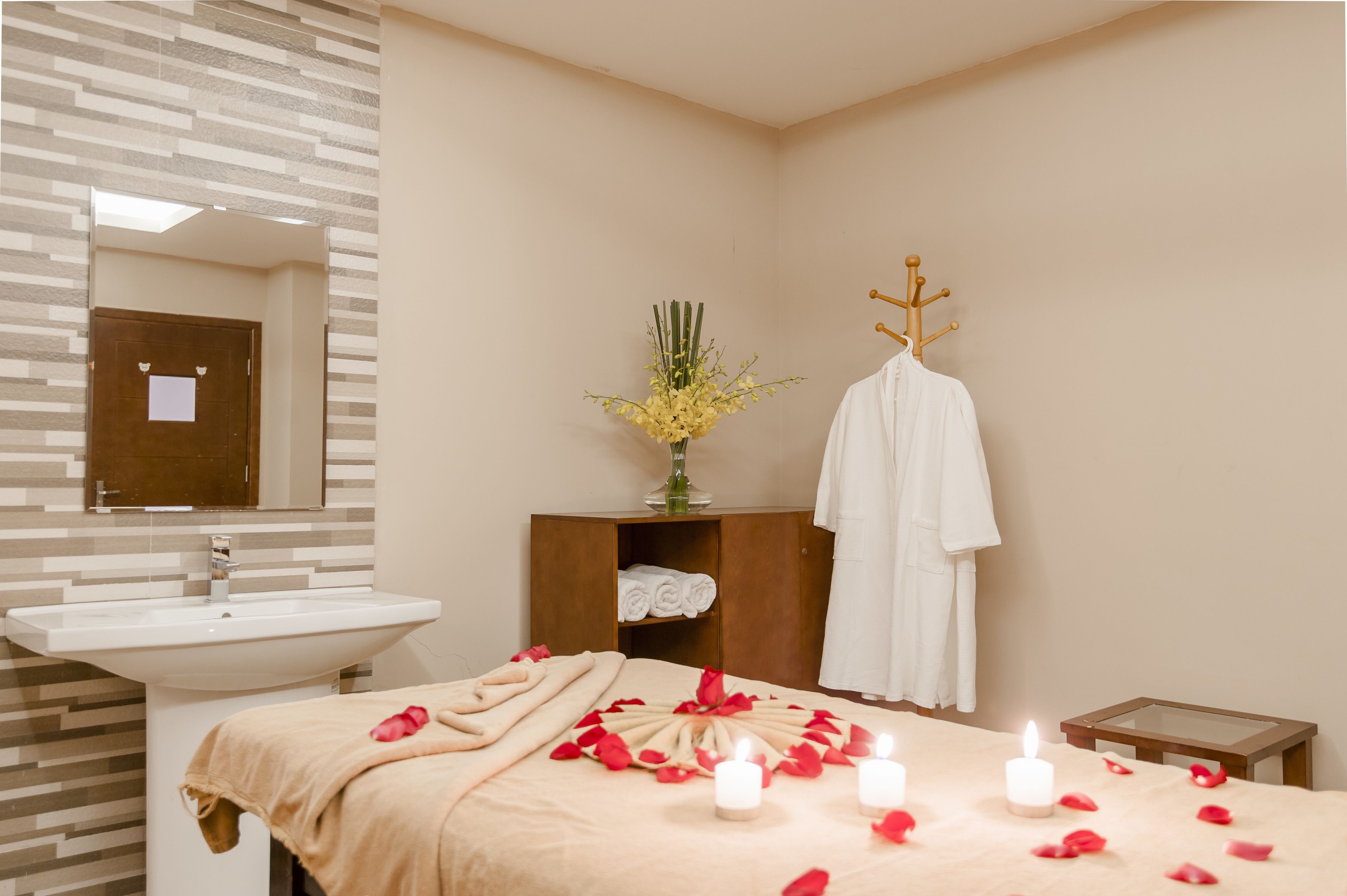 A hotel room with a bed, a bedside table, a mirror, a sink, and a wooden cabinet.