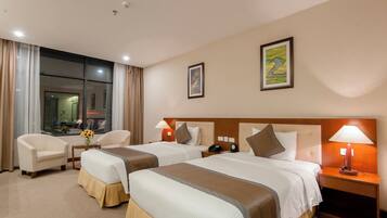 A hotel room with two beds, a sitting area with a chair, a small table with a vase of flowers, and a nightstand with a lamp.