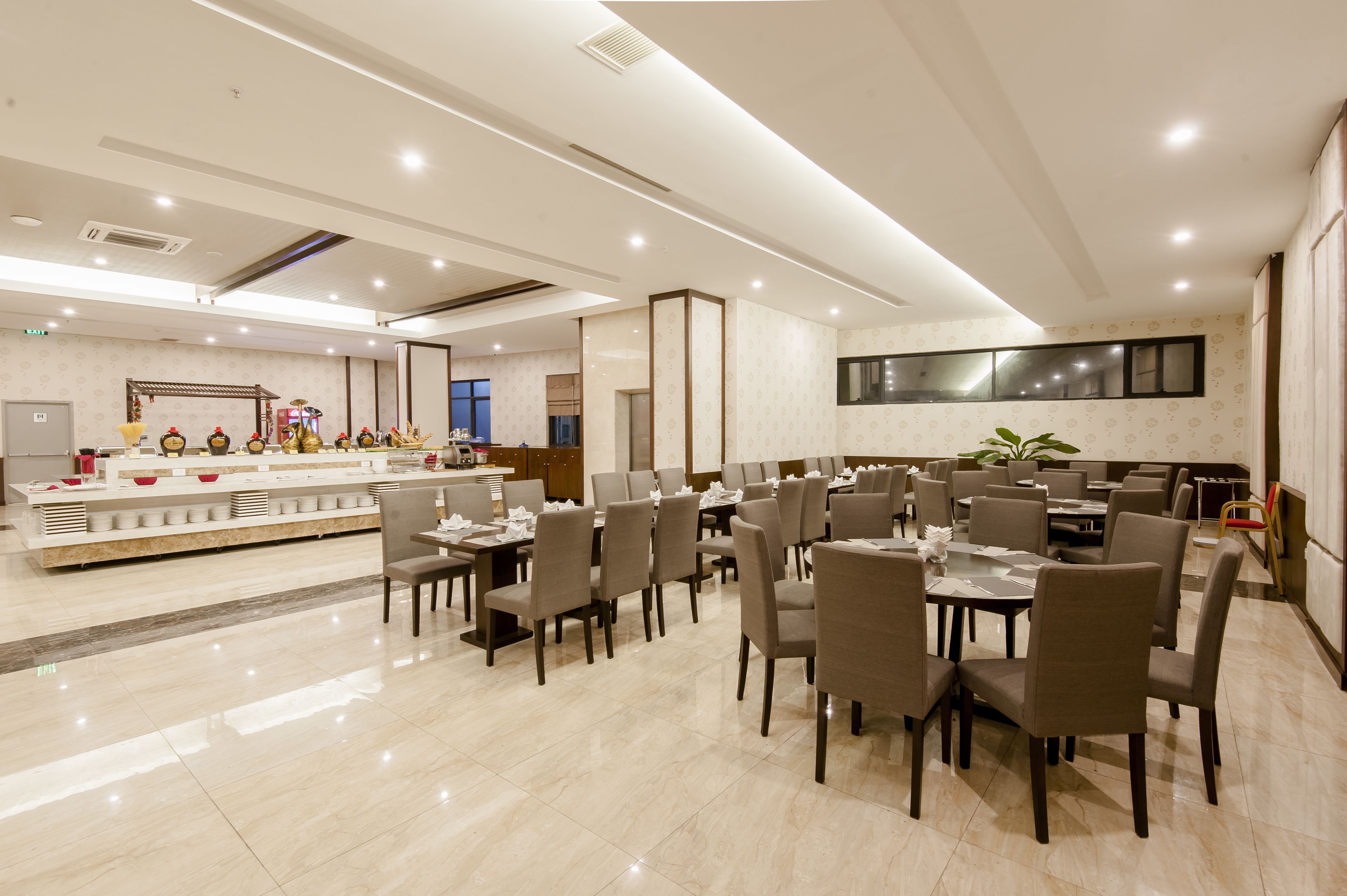 A modern dining area with multiple tables and chairs, a central counter with decorative items, and a large window with a view.