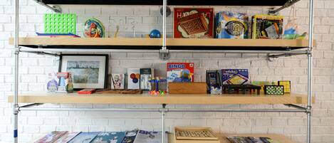 A multi-tiered metal shelving unit against a white brick wall, holding various board games and puzzles.