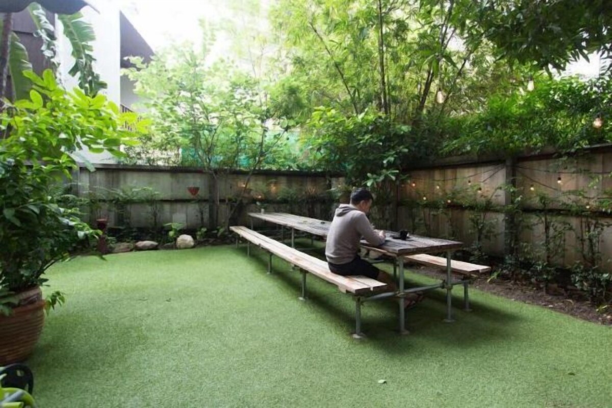 Een terras met kunstgras, houten banken en potplanten.