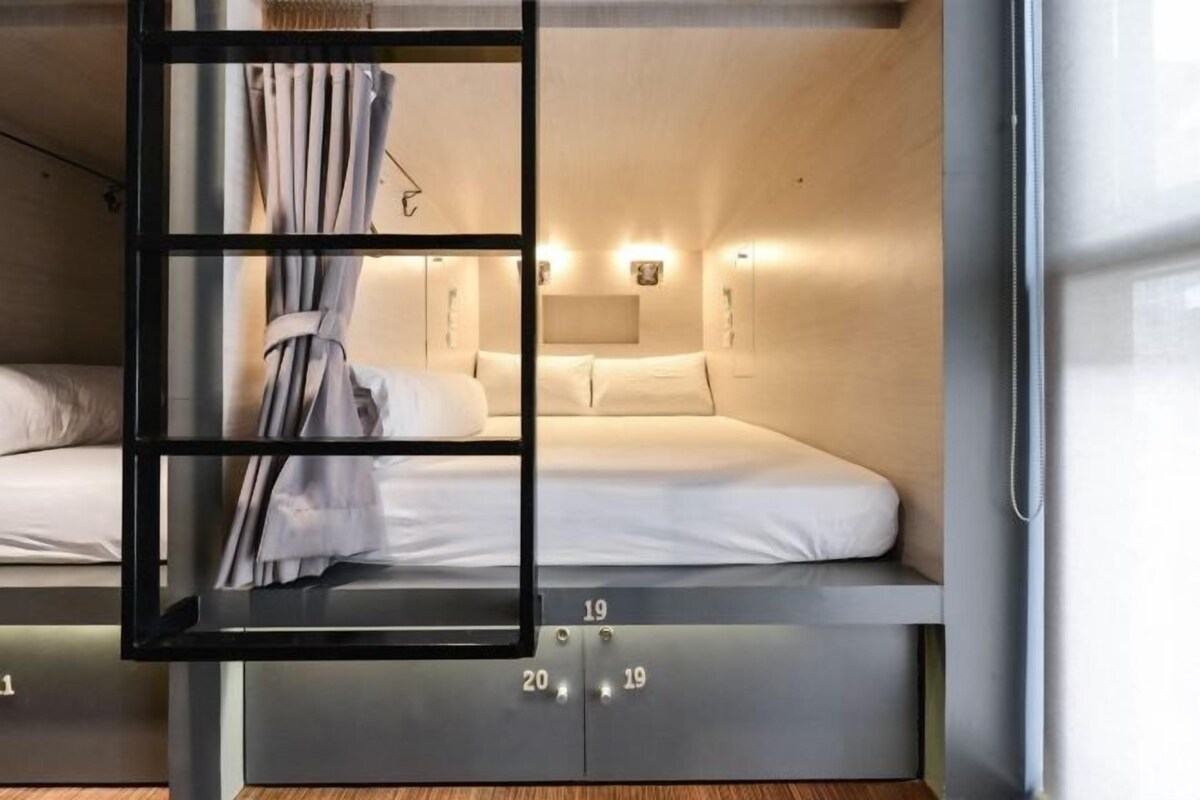 Een stapelbed met een gordijn, hoofdbord en een wandlamp.