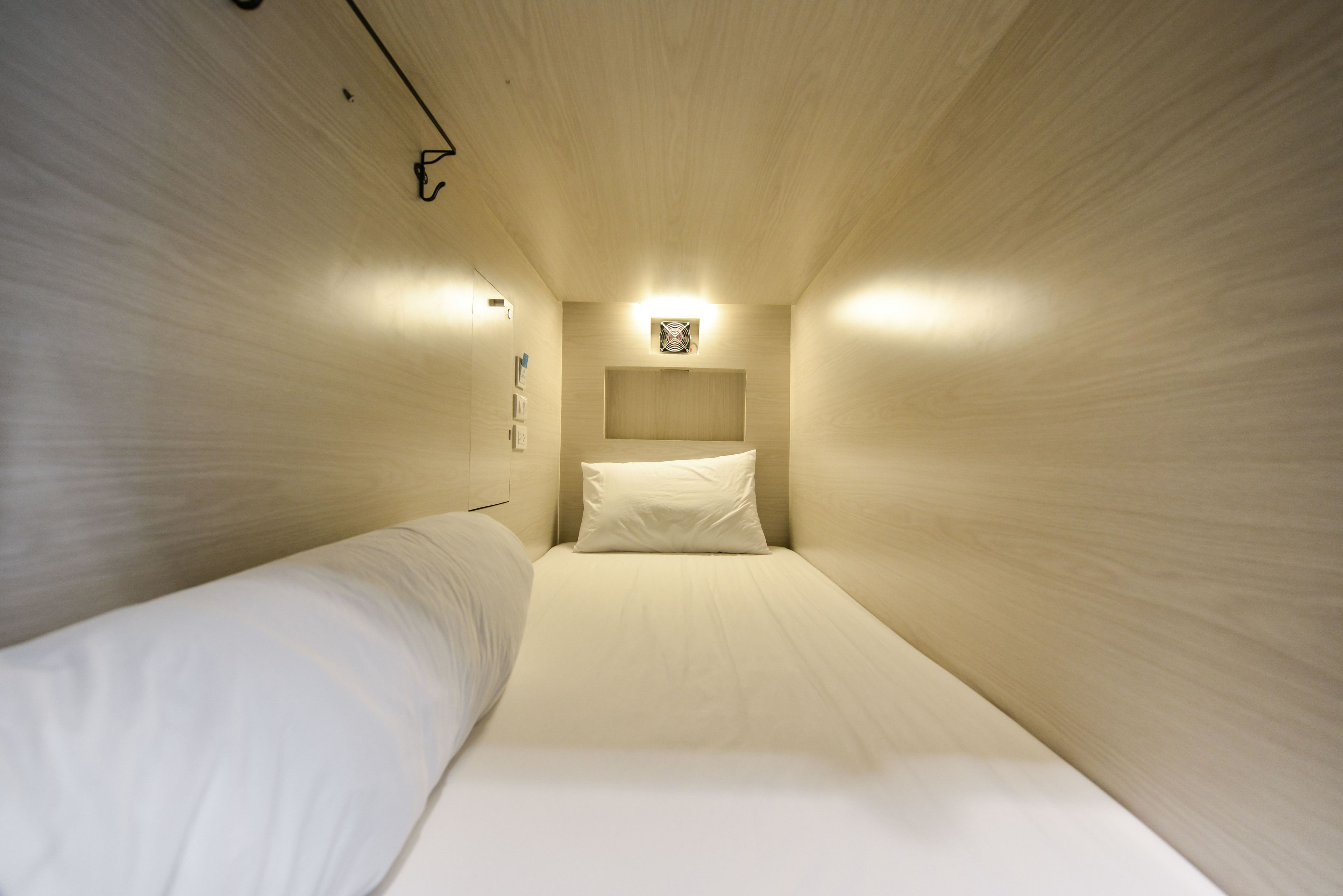 Ein schmales Zimmer mit einem Einzelbett, Holzboden und einer kleinen Wandleuchte.