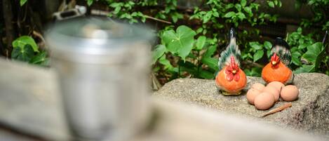 A stone ledge with a metal container, two ceramic rooster figures, and several eggs.