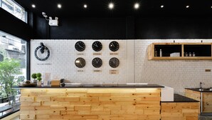 A modern kitchen with a wooden counter, a white brick wall, and clocks displaying times from various cities. - The Cube Hostel Silom (Bangkok)