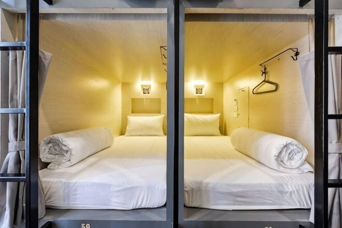 A room with two beds, each with a headboard, bedside lamps, and a hanging coat rack.