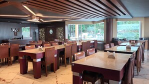Un vaste espace dédié à la salle à manger, avec de nombreuses tables et chaises, un coin bar et de grandes fenêtres qui laissent entrer la lumière naturelle.