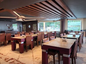 A spacious dining area with multiple tables and chairs, a bar area, and large windows providing natural light.
