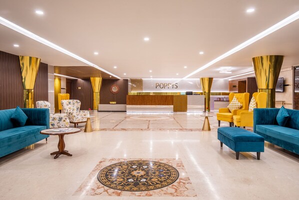 A spacious lobby with blue sofas, yellow chairs, and a central reception desk.