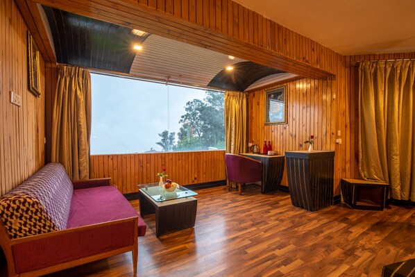 Une pièce chaleureuse avec un décor intérieur en bois, un canapé, une petite table, un coin bar et une vue sur l’extérieur grâce à une grande fenêtre.