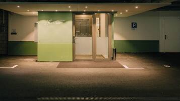 A hotel entrance with a green and white color scheme, a glass door, and a parking sign.