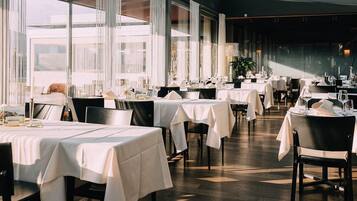 En restaurang med flera bord som är dukade för middag, stora fönster och en modern inredning.