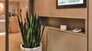 Un espace d’accueil avec une plante en pot, un comptoir d’enregistrement et un panneau indiquant « Enregistrement ».