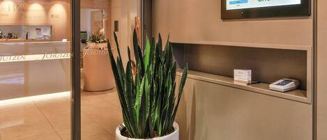 A reception area with a potted plant, a check-in kiosk, and a sign reading "Check-In".