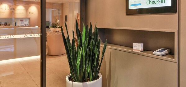 A reception area with a potted plant, a check-in kiosk, and a sign reading "Check-In". - Hotel Schützen Steffisburg (Steffisburg)