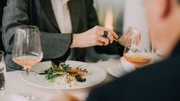 Een eettafel met borden eten, wijnglazen en een persoon die eten serveert.