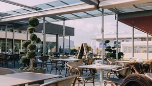 Un café en plein air avec des tables et des chaises, une grande sculpture en forme d’arbre et, au fond, un bâtiment moderne.