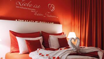 A red-themed hotel room with a bed, pillows, and a decorative wall with heart shapes and text.