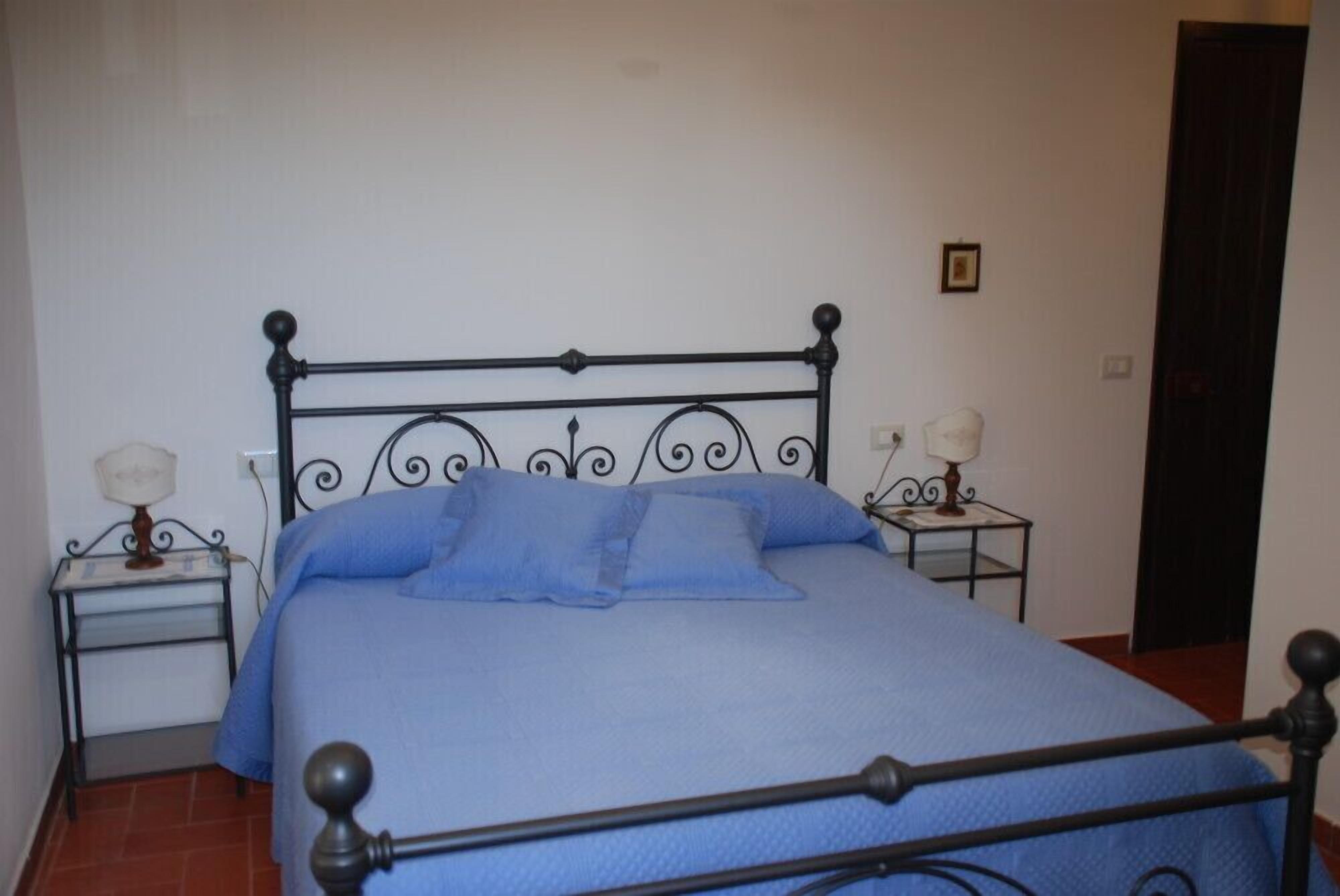 A single bed with a metal frame, two bedside tables with lamps, and a plain wall with a door.
