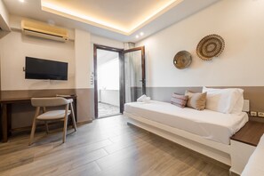 A hotel room with a bed, a desk, a chair, a television, and a balcony.