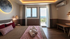 A hotel room with a bed, a bench, a wall-mounted air conditioner, and a view of the outdoors. - Asteris Village (Polygyros)