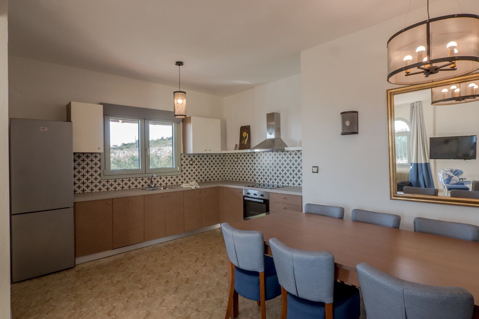 A modern kitchen with a dining area, featuring a large window, a built-in oven, and a chandelier.