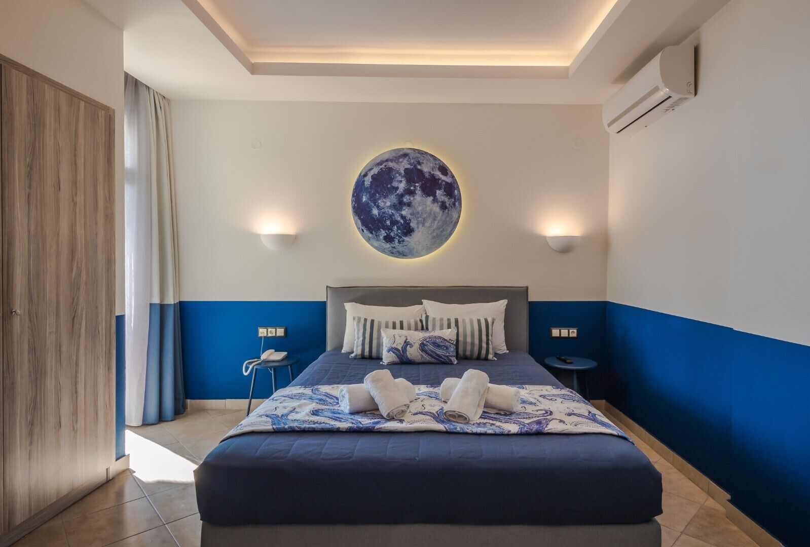 Une chambre moderne avec un grand lit, une décoration murale circulaire sur le thème de la lune et une table de chevet avec un téléphone.