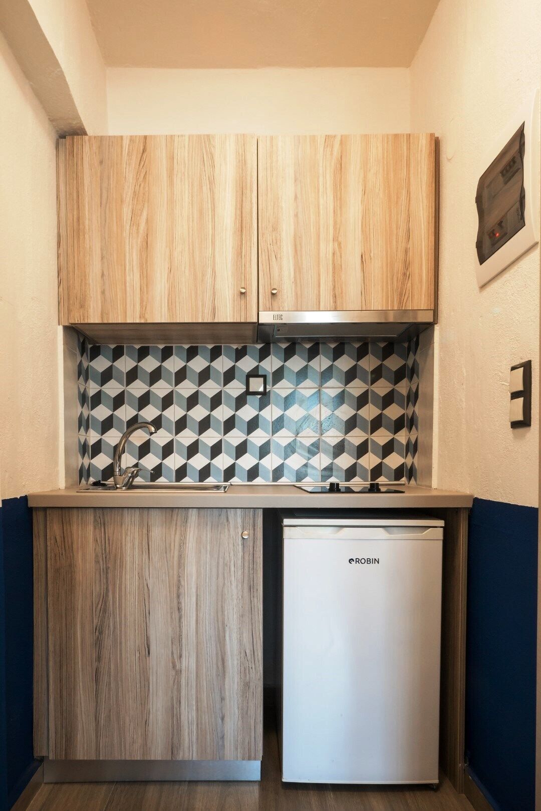 Una cocina compacta con armarios de madera, un salpicadero geométrico y un lavavajillas integrado.