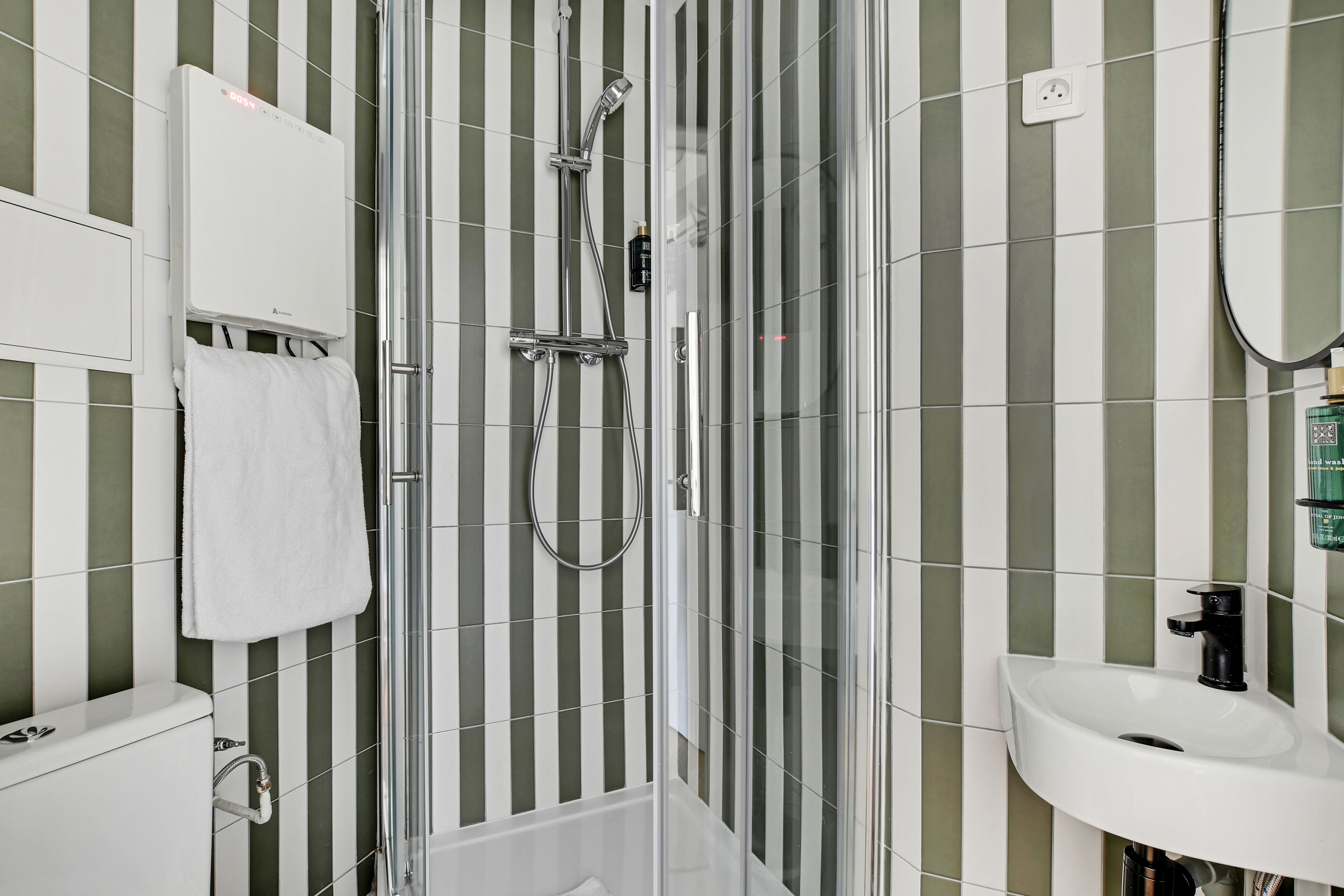 A modern bathroom with a glass-enclosed shower, a white sink, and striped green and white tiles.