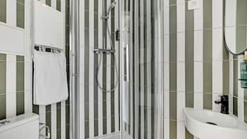 A modern bathroom with a glass-enclosed shower, a white sink, and striped green and white tiles.