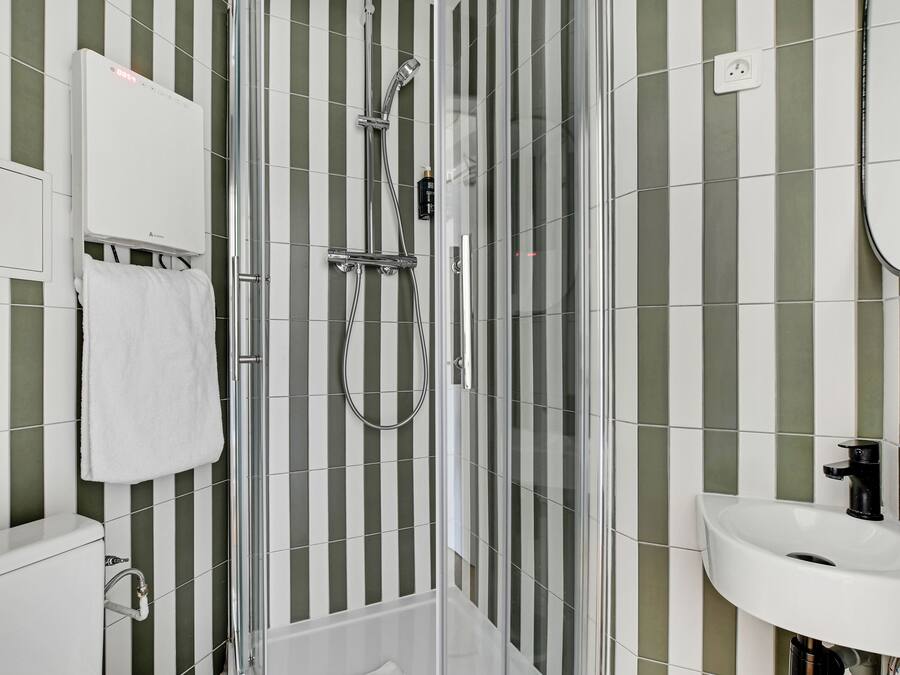 A modern bathroom with a glass-enclosed shower, a white sink, and striped green and white tiles.