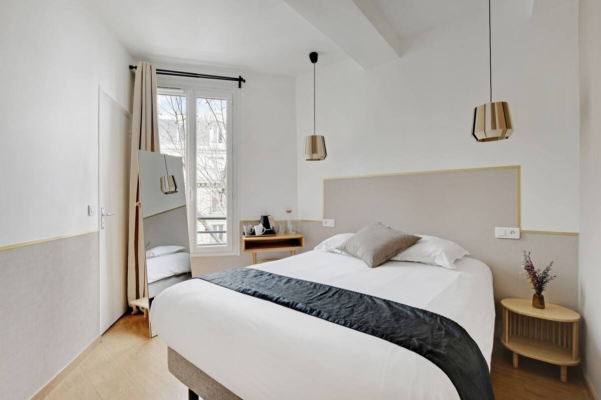 A modern hotel room with a large bed, bedside table, and a window with curtains.