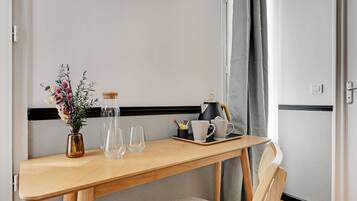 A wooden table with a vase of flowers, two glasses, a coffee pot, and a tray with cups and a small container.