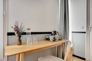 A wooden table with a vase of flowers, two glasses, a coffee pot, and a tray with cups and a small container.