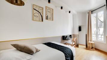 A modern bedroom with a large bed, a desk, and a chair. There are abstract wall art pieces and a window with curtains.
