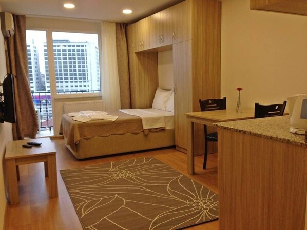 A compact hotel room with a bed, a small desk, and a window with a city view. - Stay Suites (Istanbul)