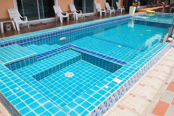A rectangular swimming pool with blue tiles, surrounded by white plastic chairs and a tiled deck.