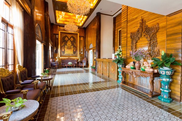 A spacious lobby with ornate wooden paneling, a patterned tiled floor, and a reception area with traditional decor.