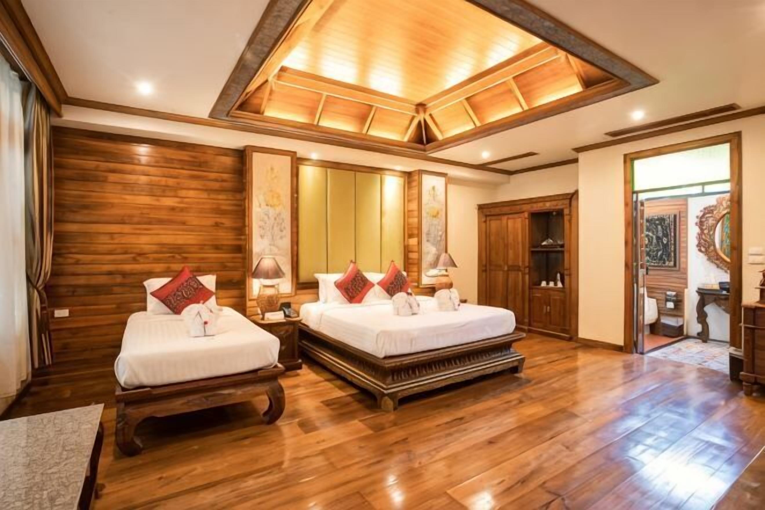 A hotel room with two beds, wooden flooring, a large mirror, and a wooden ceiling.