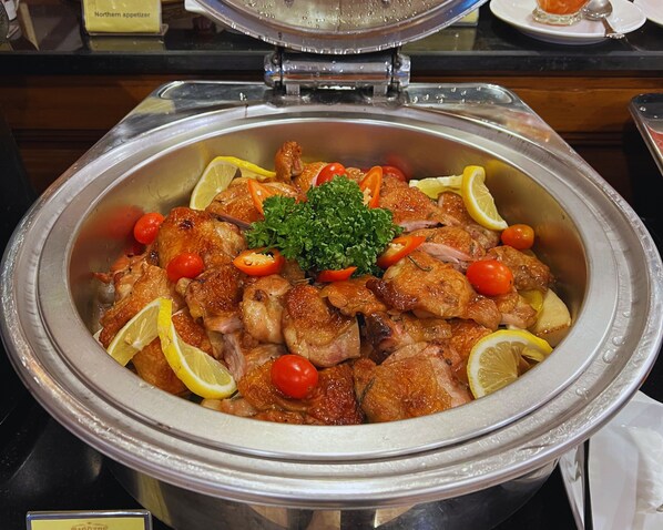 A buffet with a variety of dishes, including a large pot of roasted chicken garnished with lemon slices and cherry tomatoes. - Pingviman Hotel (Chiang Mai)
