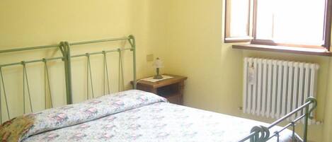 A single bed with a floral bedspread in a room with yellow walls, a window, and a radiator.