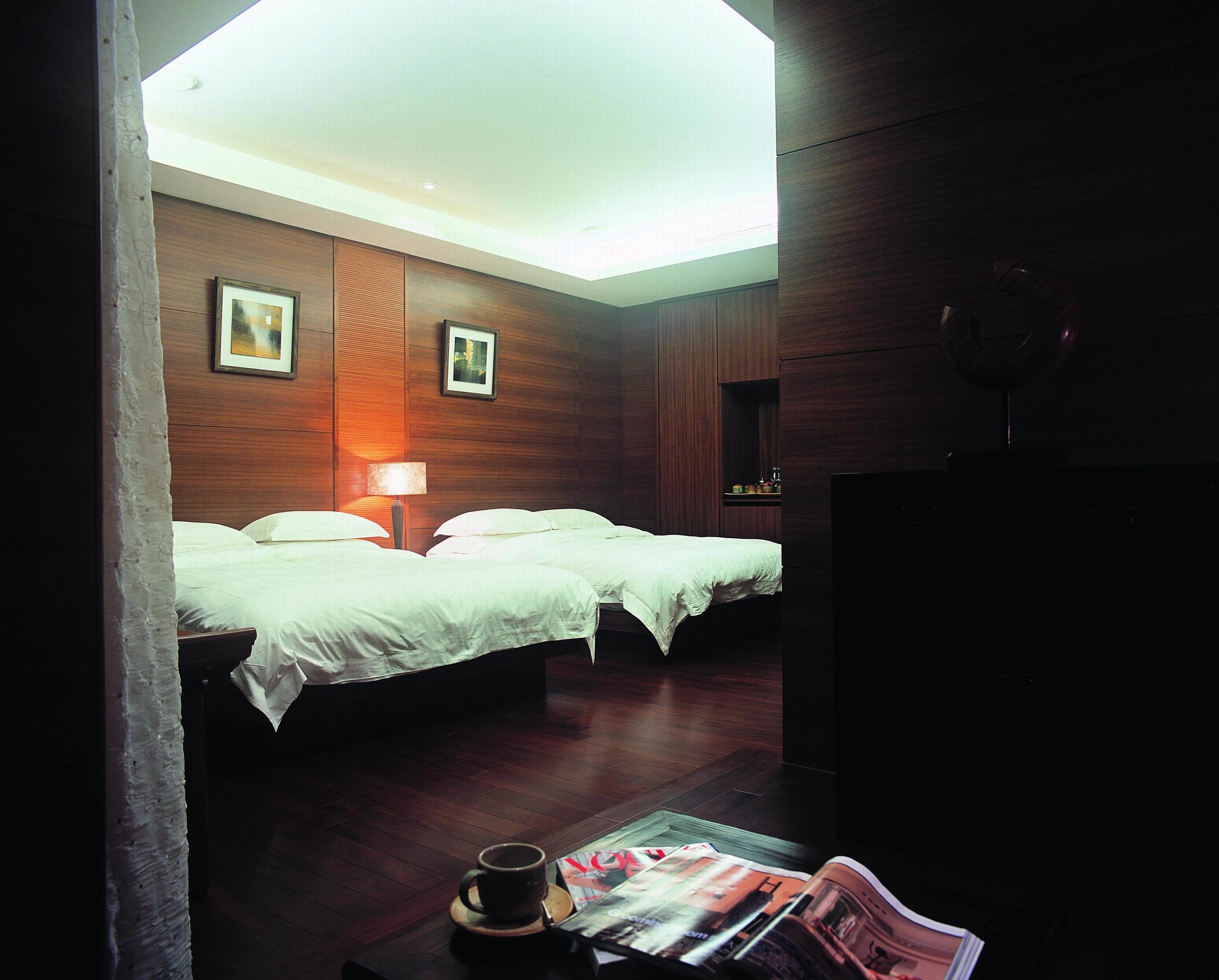 A hotel room with two beds, a lamp, a magazine on a table, and a ceiling light.