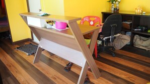 A room with a wooden desk, a chair, a small table with a vase, and a shelf with items. - BB House Beach Resort (Pattaya)