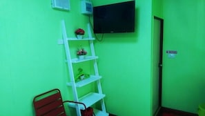 A room with green walls, a white shelf with decorative items, a red chair, and a flat-screen TV mounted on the wall.