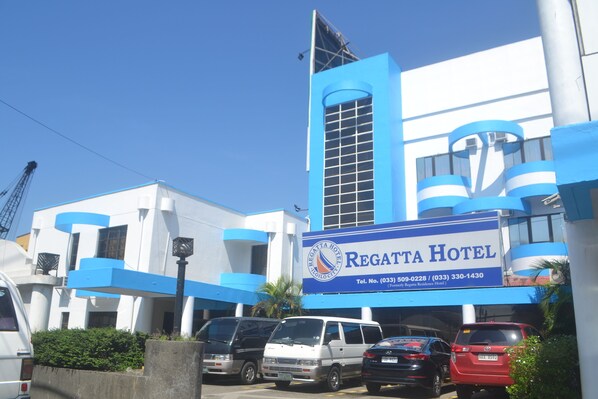 Hotel com fachada azul e branca, uma placa com o nome do hotel e vários carros estacionados na frente.