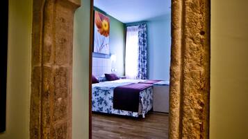 A hallway leading to a bedroom with a wooden floor, a bed with a floral bedspread, and a large flower painting on the wall.