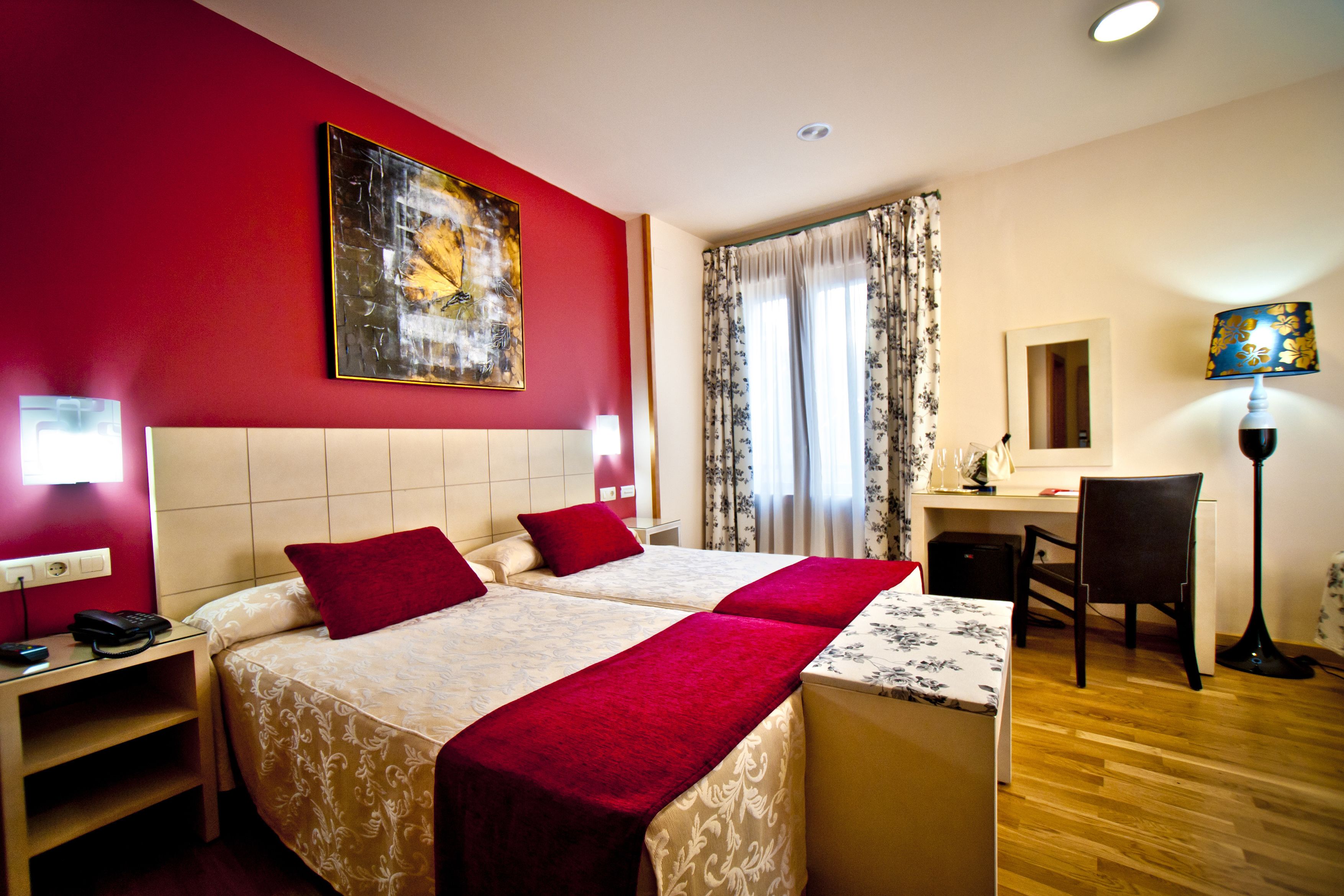 Habitación de hotel con dos camas, un escritorio, una silla, una lámpara y un cuadro en la pared.