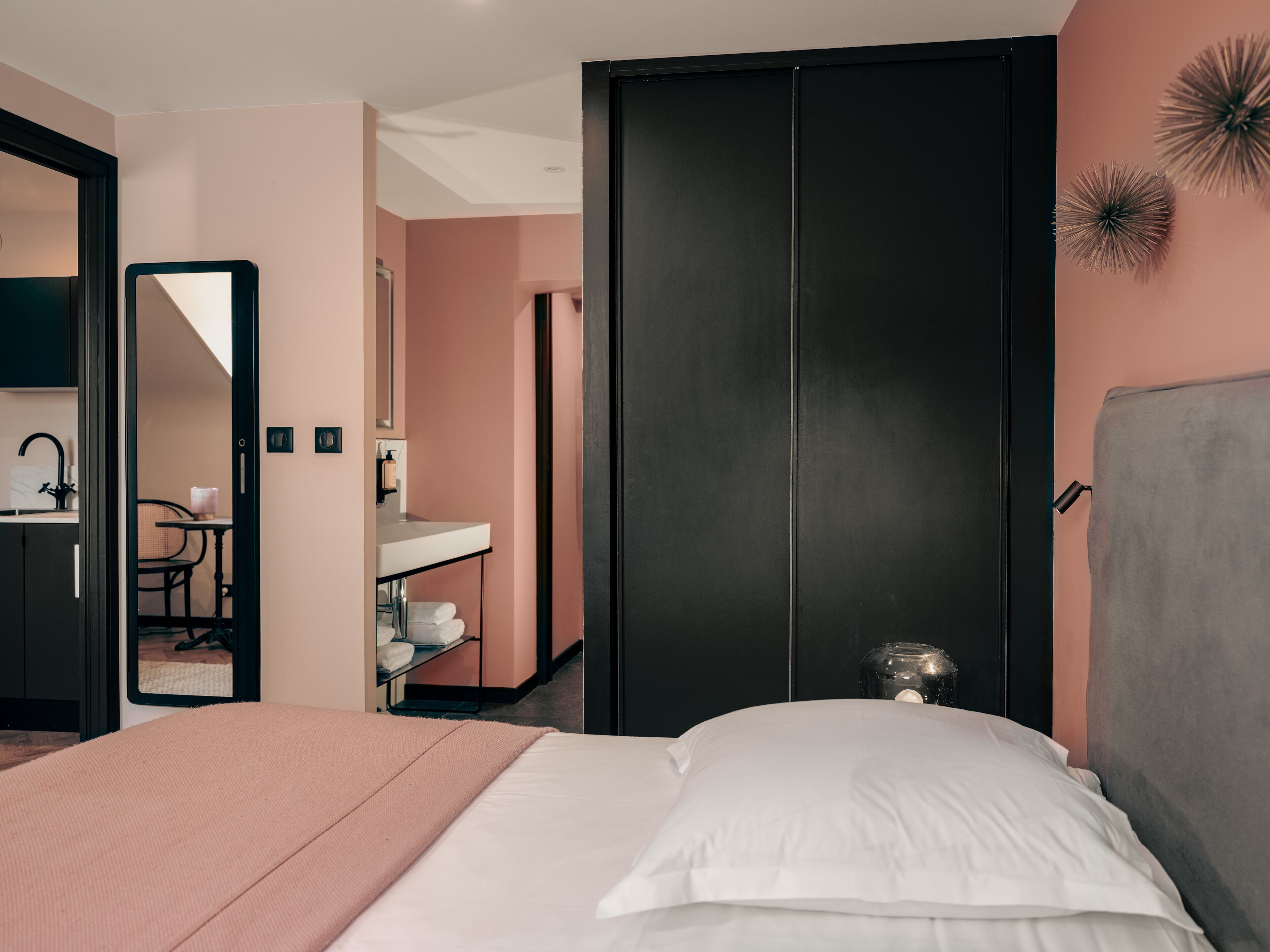 A bedroom with a bed, a bedside table, a mirror, a wardrobe, and a bathroom visible through an open door.